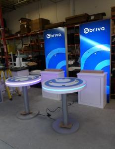 (2) 36" W x 96" H Backlit Lightboxes with Tension Fabric Graphics, (2) Custom Counters with Locking Storage, (2) Monitor Mounts, and (2) MOD-1453 Wireless Bistro Charging Tables with Graphics